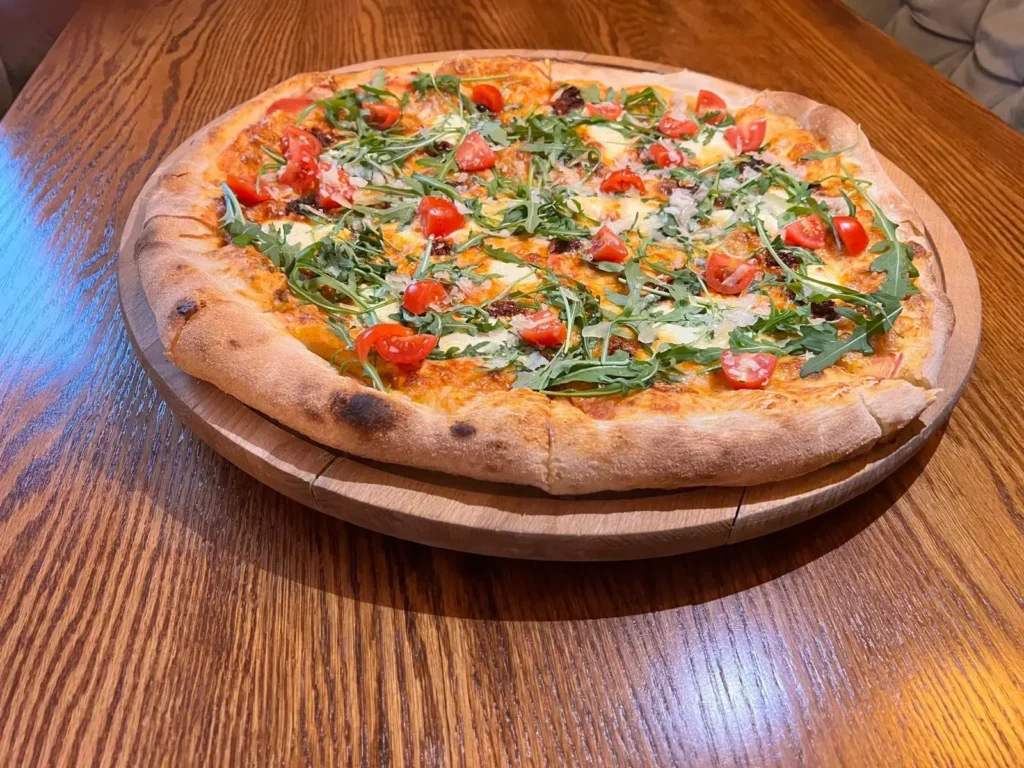 Pizza z rukolą i pomidorkami koktajlowymi na drewnianej desce